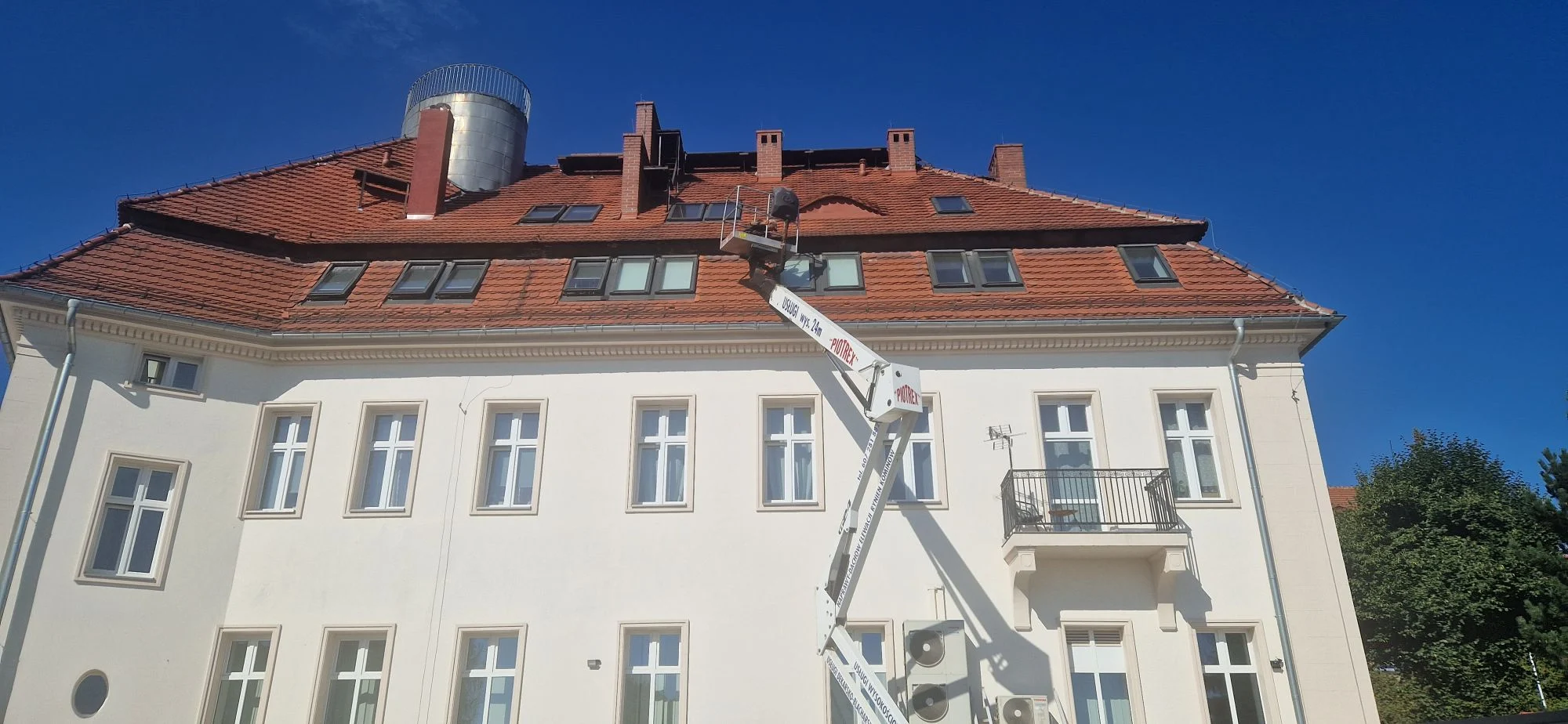 Podnośnik koszowy PIOTREX przy dachu kamienicy z czerwonej dachówki
