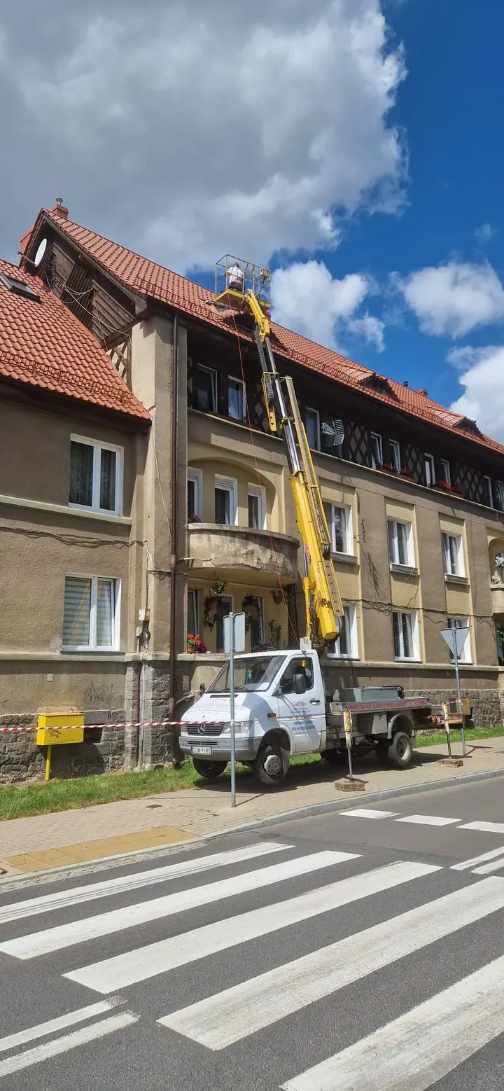 Żółty wysięgnik podnośnika przy czerwonym dachu kamienicy